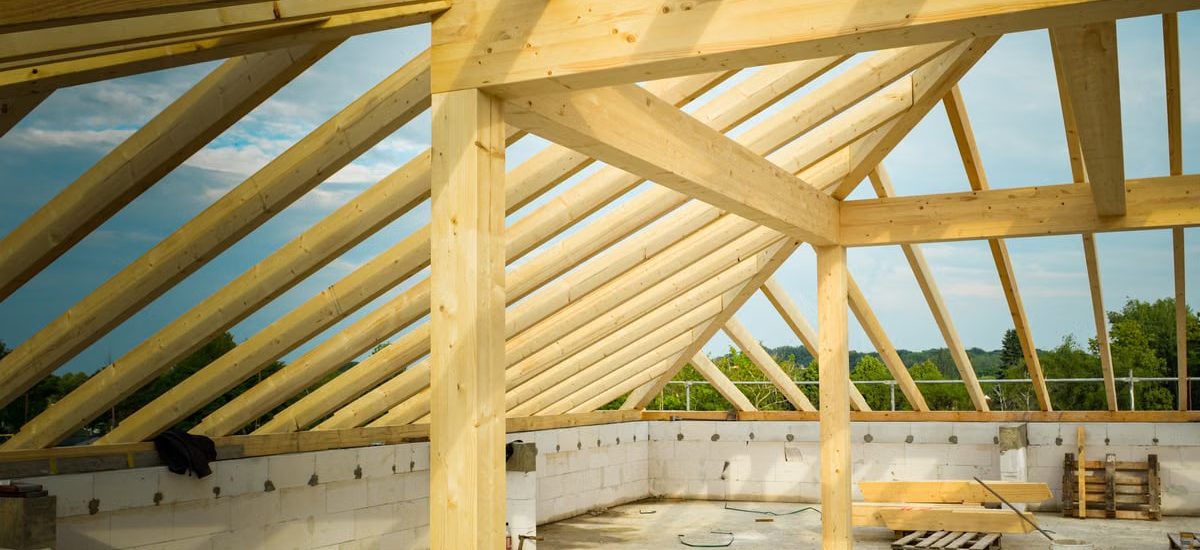 Unfinished construction site with a focus on wooden roof trusses under a clear sky.