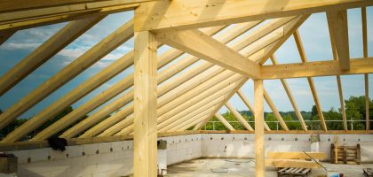 Unfinished construction site with a focus on wooden roof trusses under a clear sky.