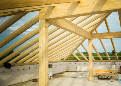 Unfinished construction site with a focus on wooden roof trusses under a clear sky.
