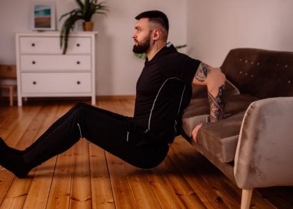 A bearded man in black fitness attire exercising at home, showcasing arm tattoos and a healthy lifestyle.