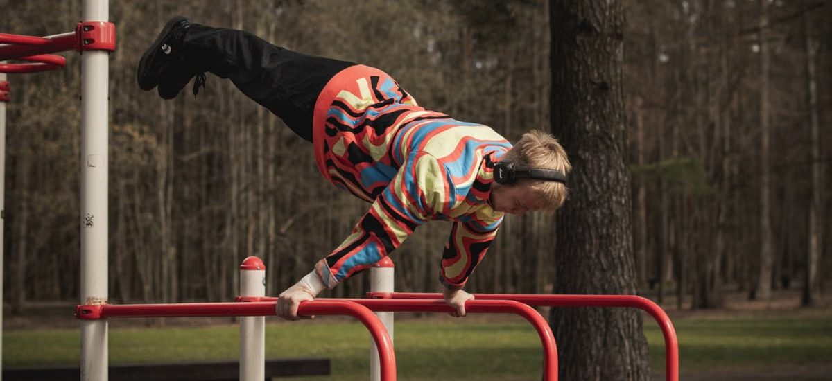 Young man wearing colorful outfit doing calisthenics on red bars in Vilnius park.