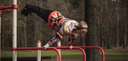Young man wearing colorful outfit doing calisthenics on red bars in Vilnius park.