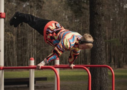 Young man wearing colorful outfit doing calisthenics on red bars in Vilnius park.